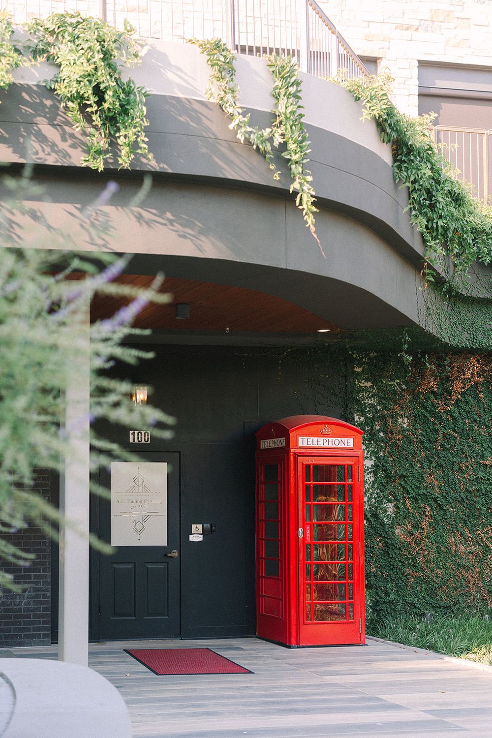 A classic red British telephone booth sits in front of a black door with ivy-covered walls at an elegant entrance.