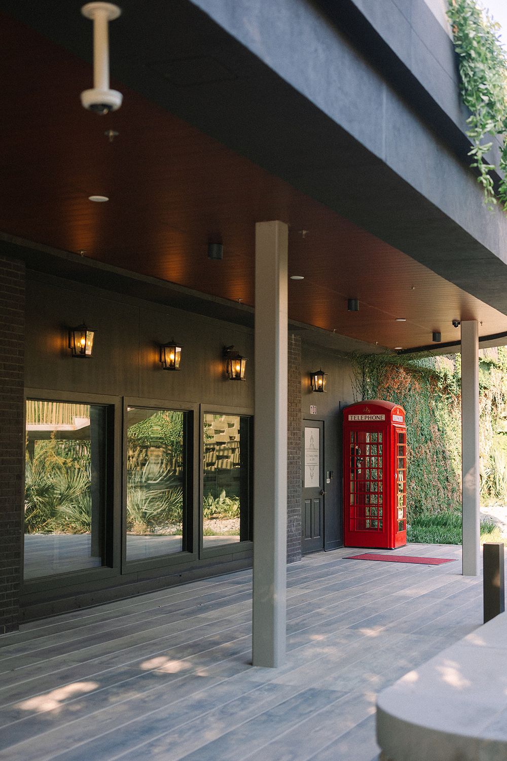 A long covered outdoor corridor with modern architecture features a distinctive red British-style phone booth against grey walls.