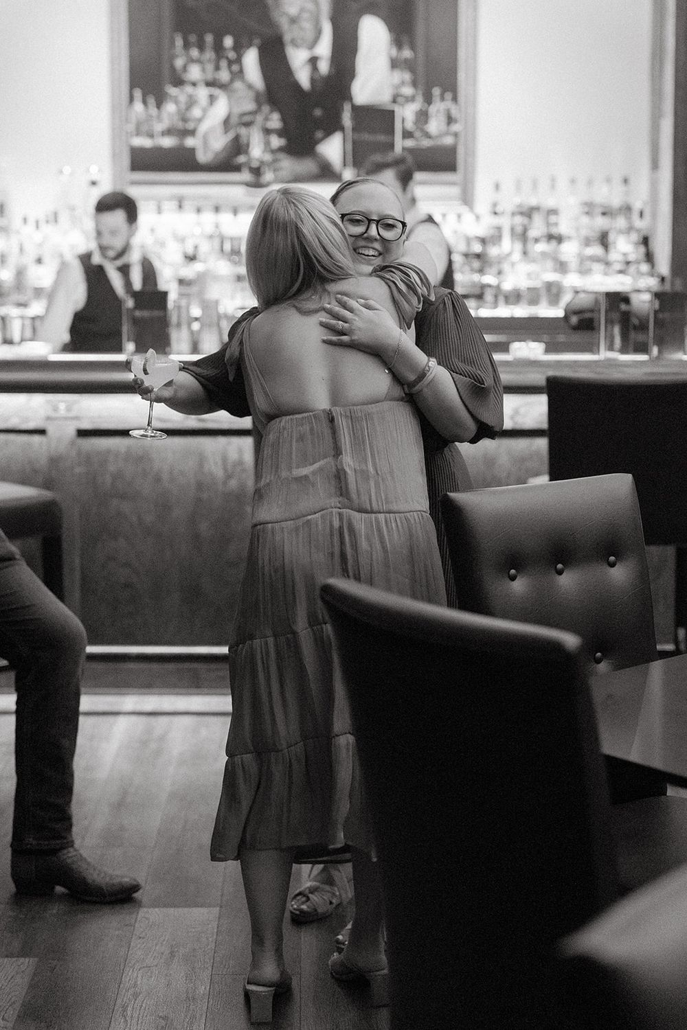 Black and white photo of patrons embracing at an upscale bar with bartenders visible in the background.