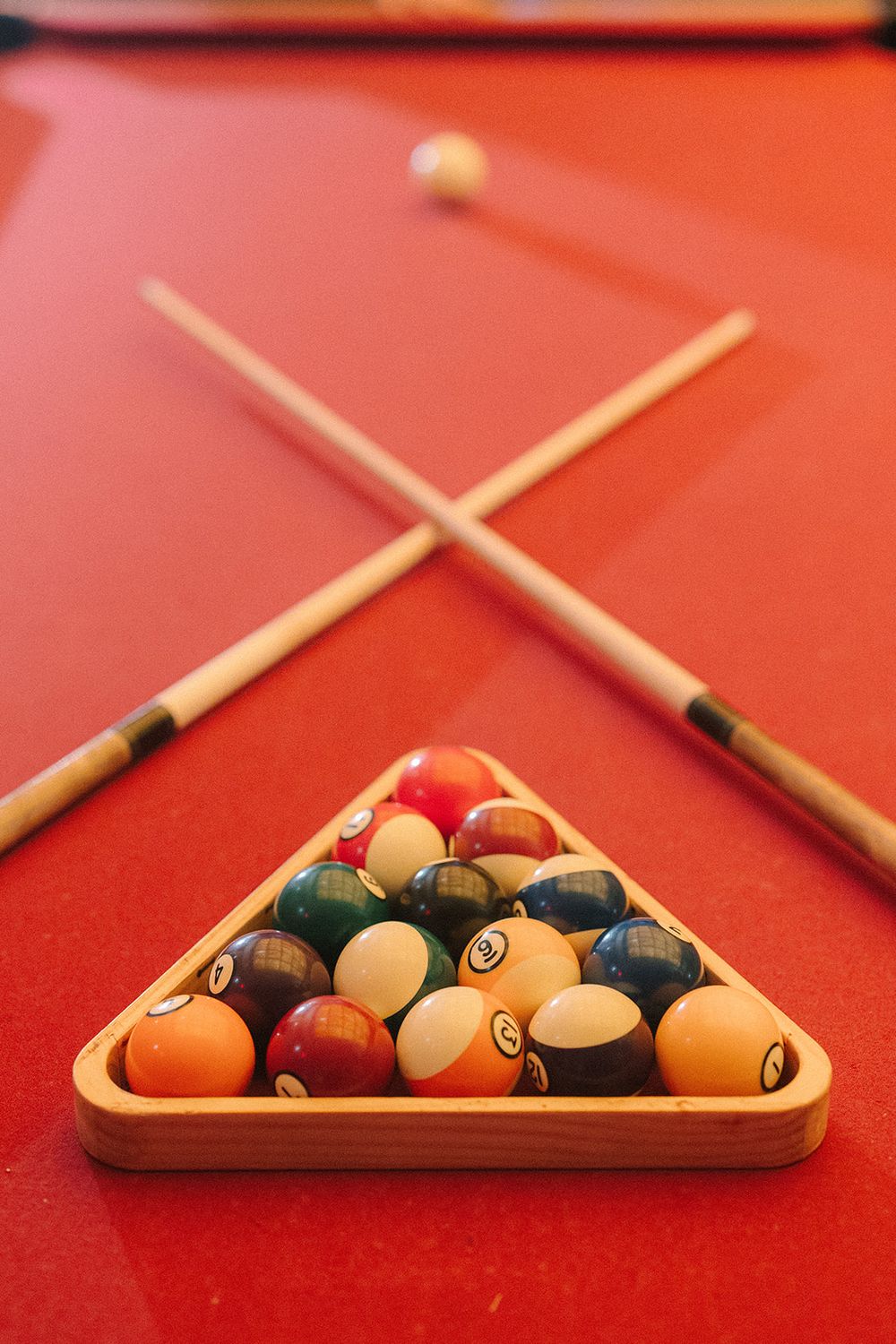 Pool balls arranged in a wooden triangle rack with crossed cue sticks on a red felt billiards table.