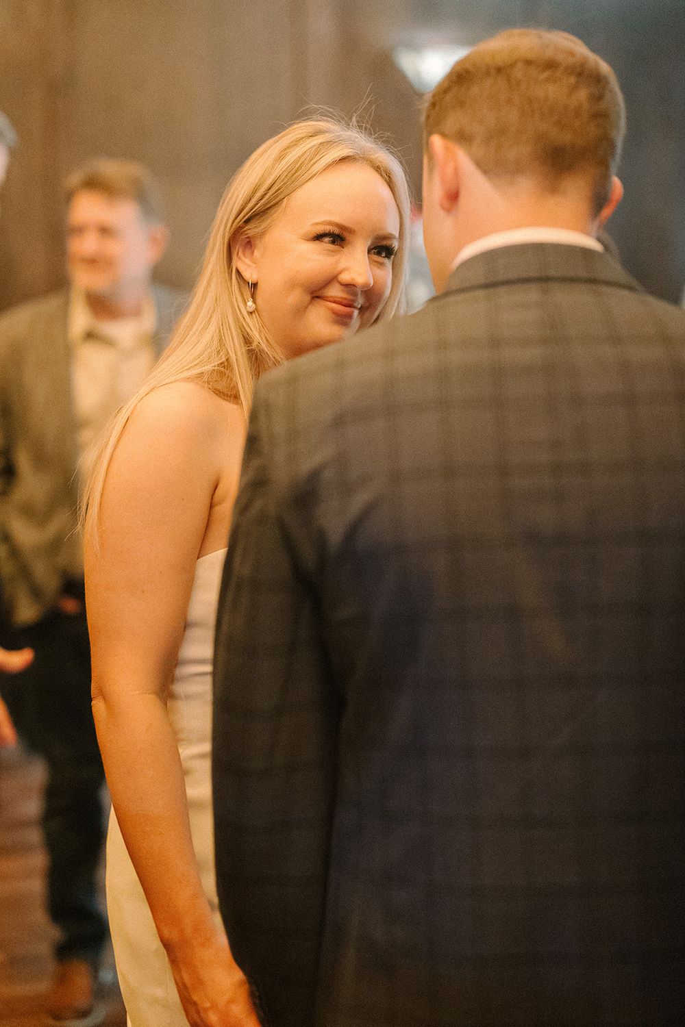 A couple shares a tender moment at a wedding reception as they gaze at each other in warm lighting.