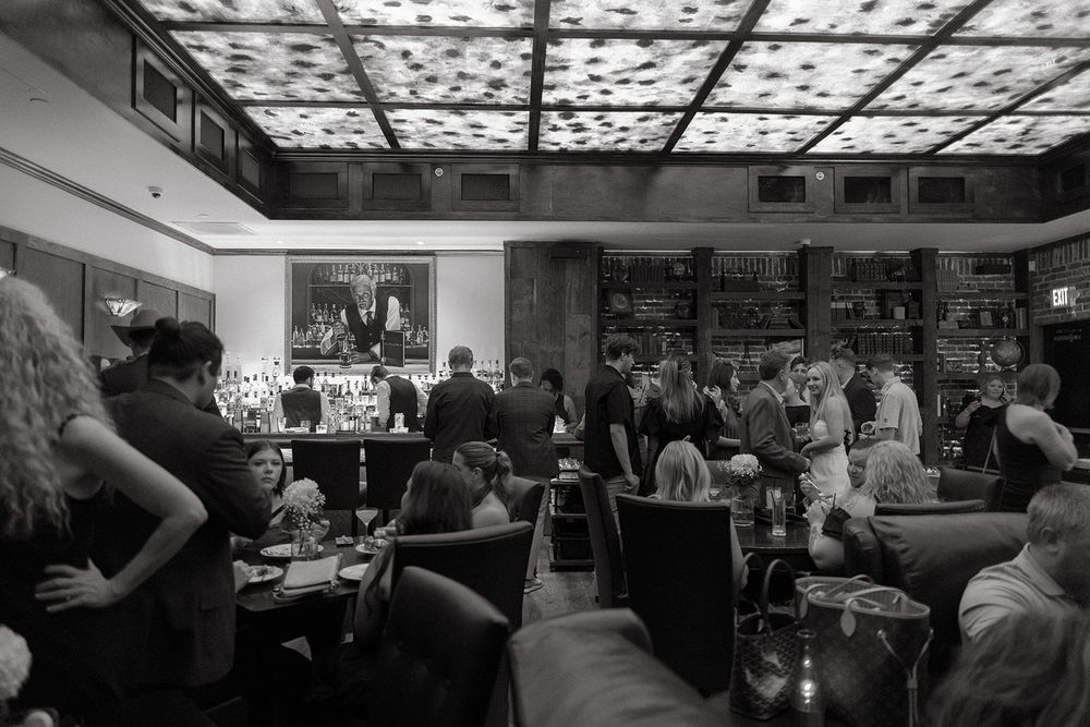 Restaurant patrons dining under an illuminated decorative ceiling in a busy upscale establishment, captured in black and white.