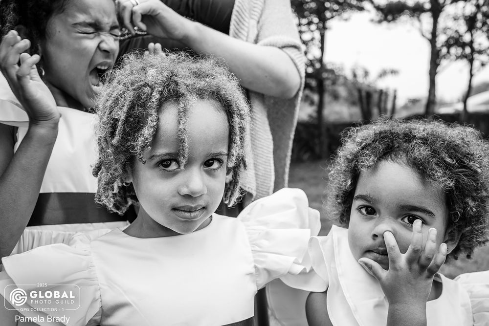Three children in black and white showing different emotional expressions while posing together outdoors.