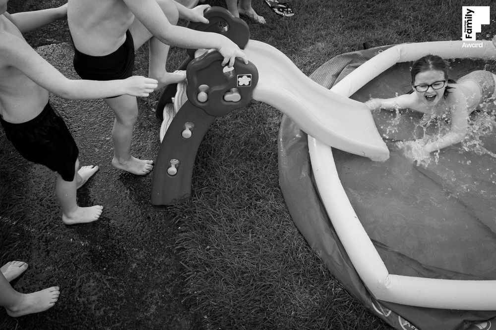 Children splashing and playing in an inflatable backyard pool on a sunny day.