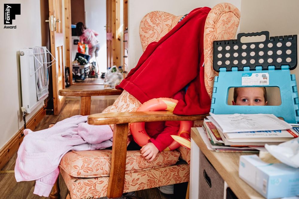 Red blanket on chair next to blue playpen with toys scattered in sunlit hallway.