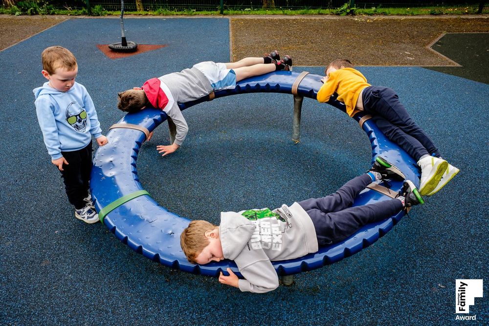 Children playing on a circular playground equipment against a blue rubber surface outdoors.