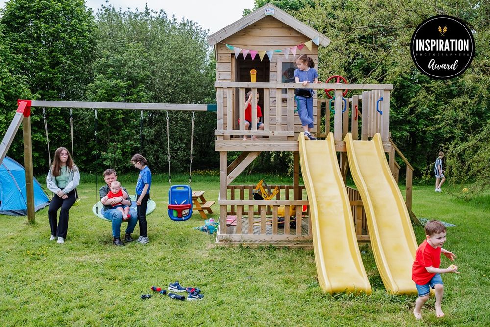 Children playing on a wooden playground structure with slides and swings in a backyard setting.