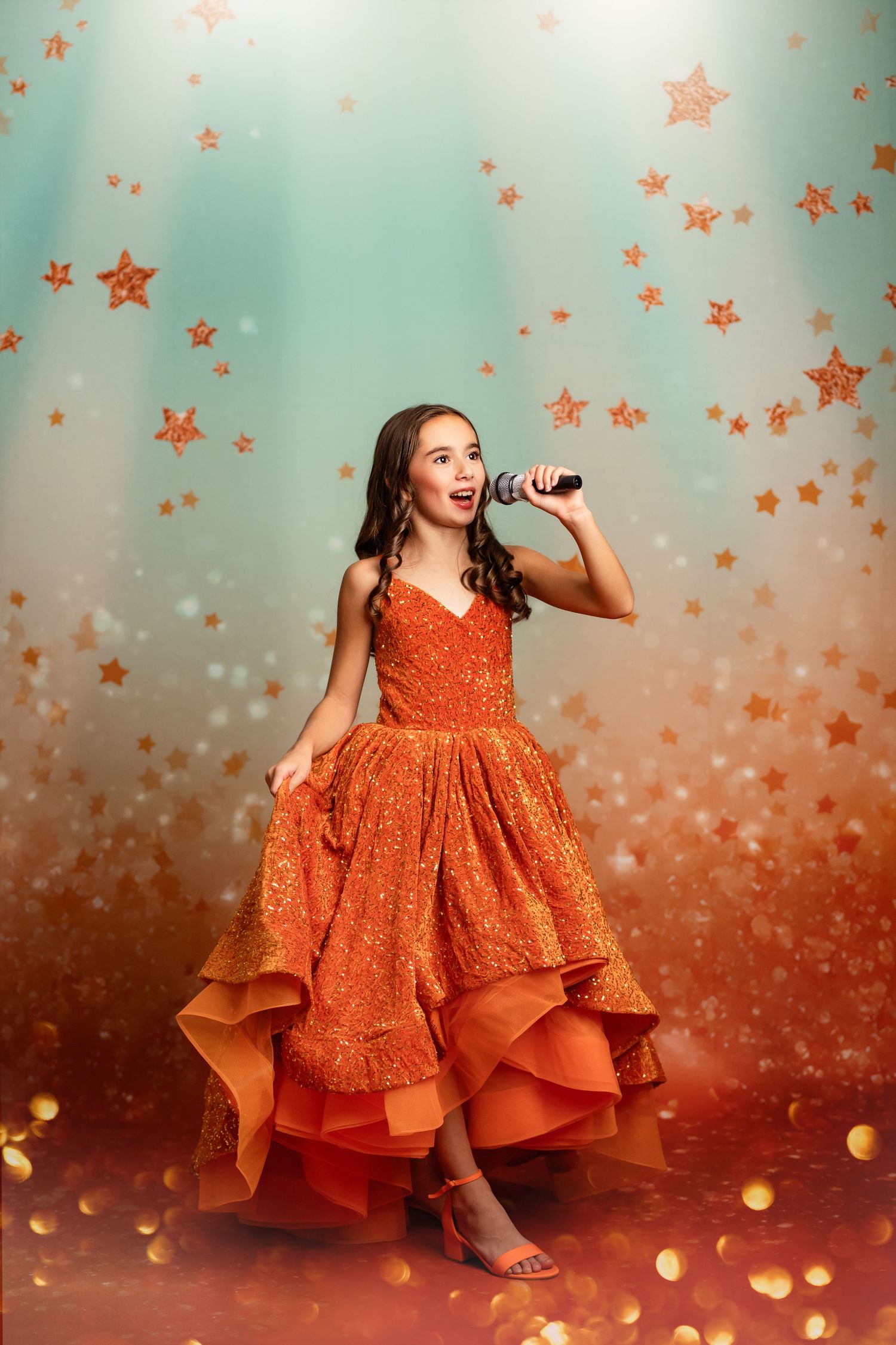 Flowing copper-colored ballgown with tulle layers photographed against dramatic studio backdrop.