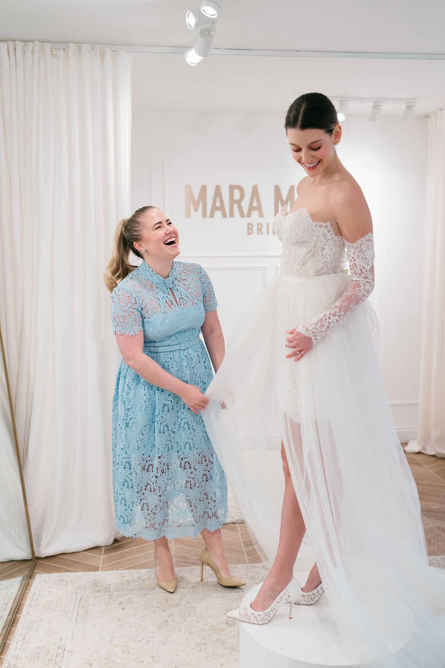 A young girl in a light blue lace dress interacts playfully with wedding gowns in a bridal boutique.