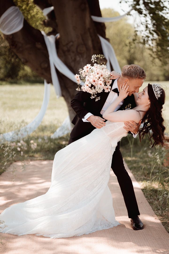 Romantic wedding couple in white dress and black tuxedo perform graceful dance dips outdoors.