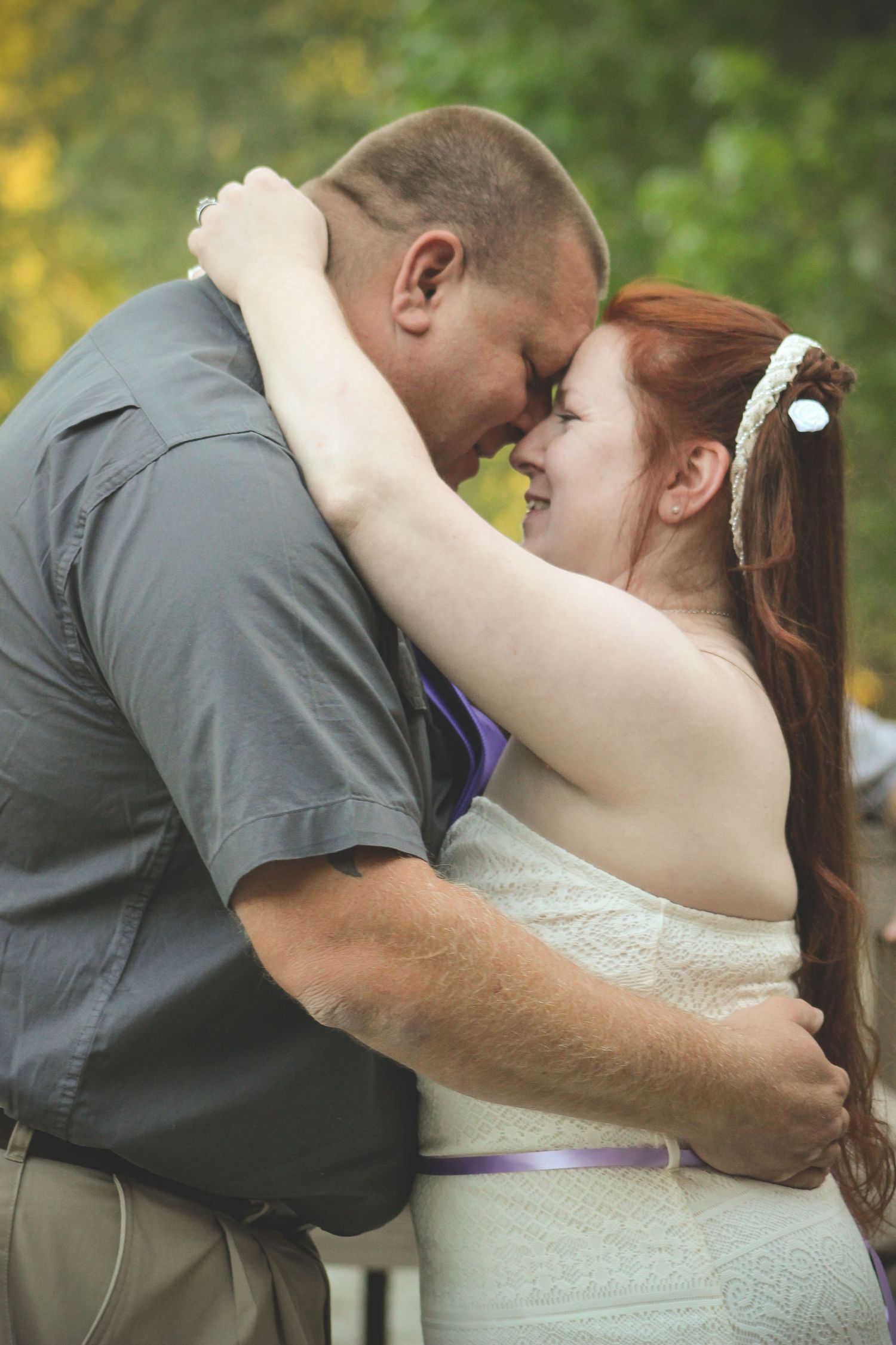 Romantic embrace between couple in plaid and white against natural backdrop.