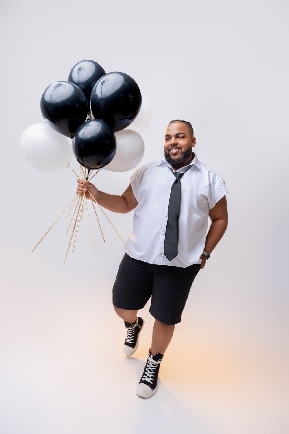 Person in business casual attire holding black and white balloons in a minimalist photoshoot against a light background.