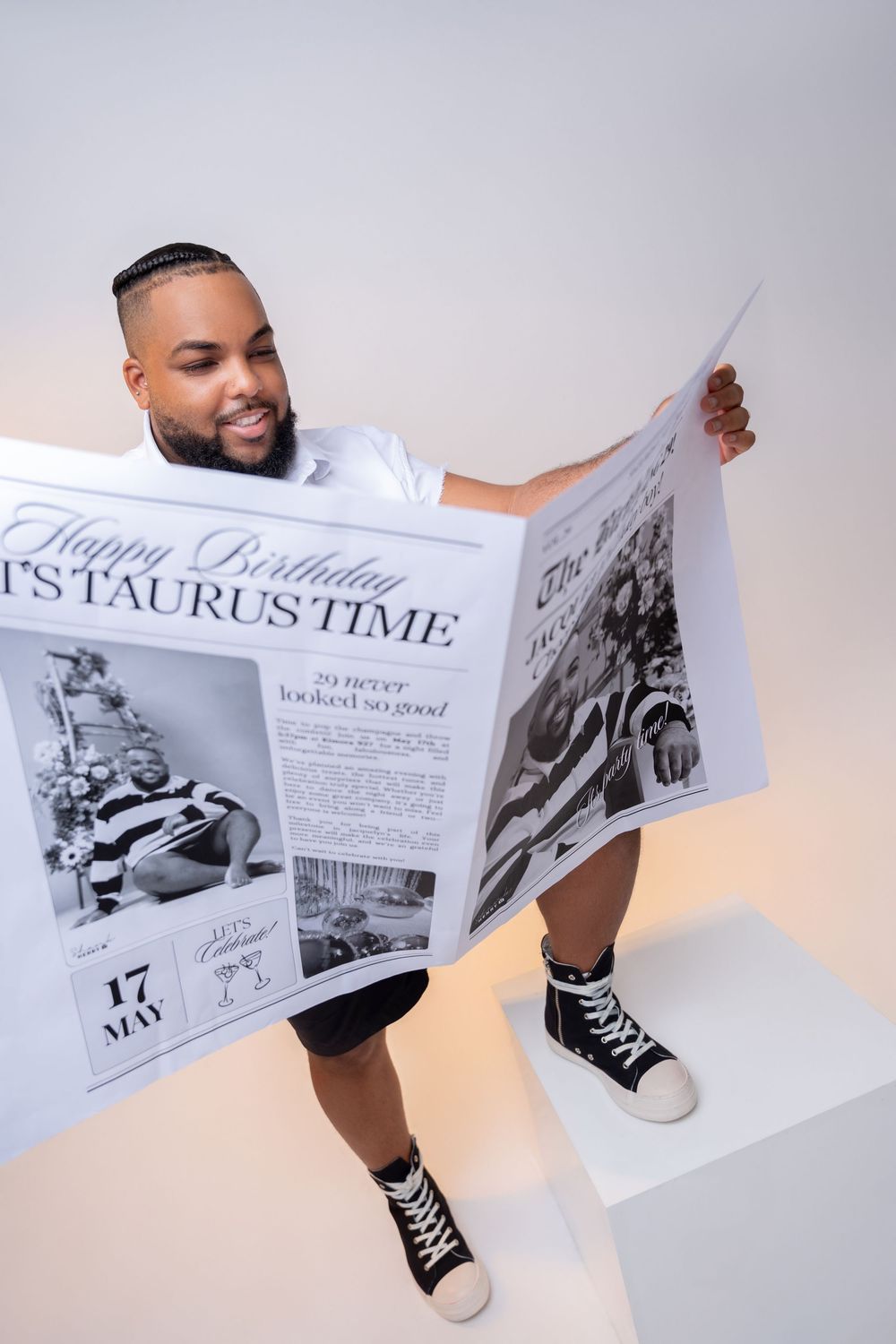 Person in white shirt and black sneakers holds up a large newspaper with 'Taurus Time' headline against white background.