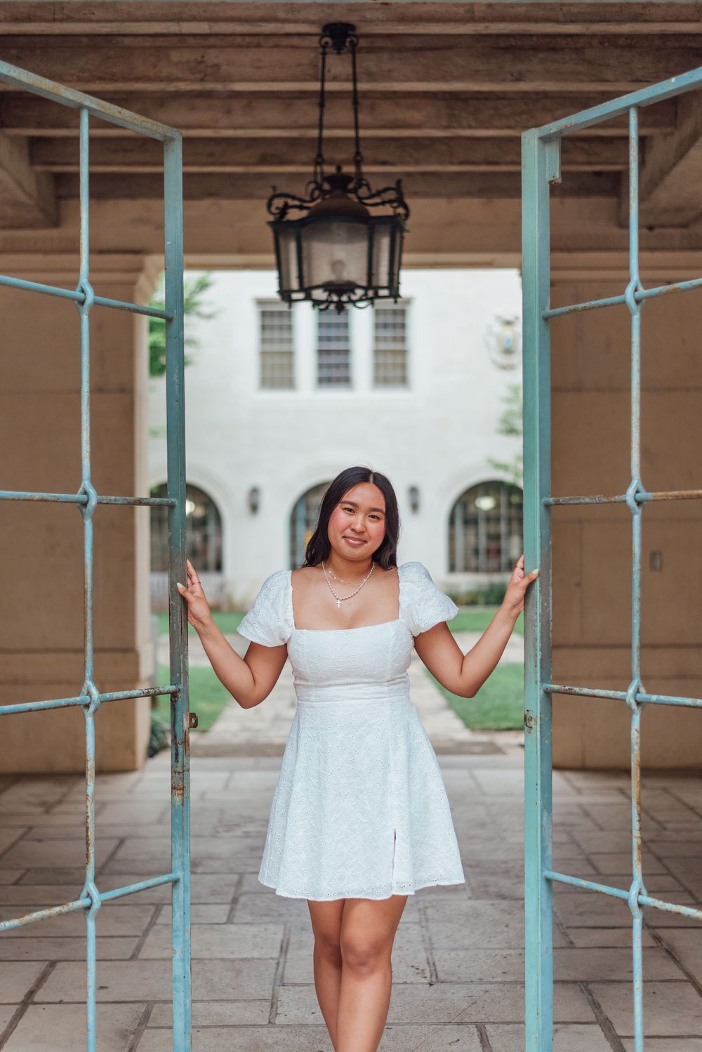 A white summer dress complements the architectural features of a covered walkway with mint-colored railings and hanging lantern.