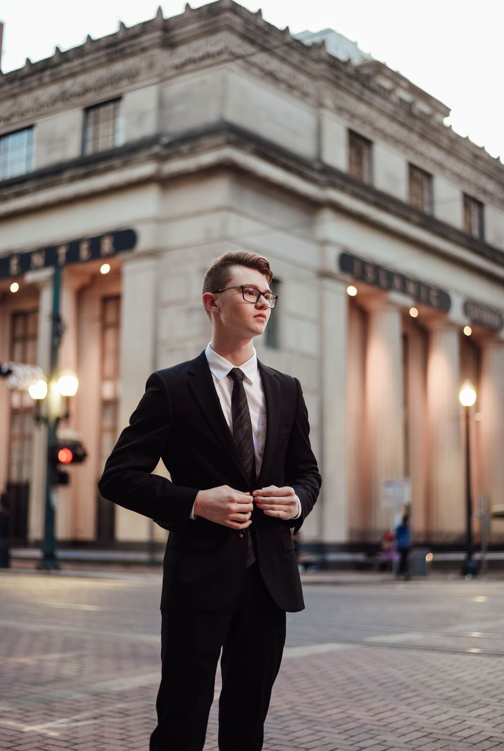 High school senior boy in a suit standing in downtown Houston at sunset, showcasing elegance and urban charm.