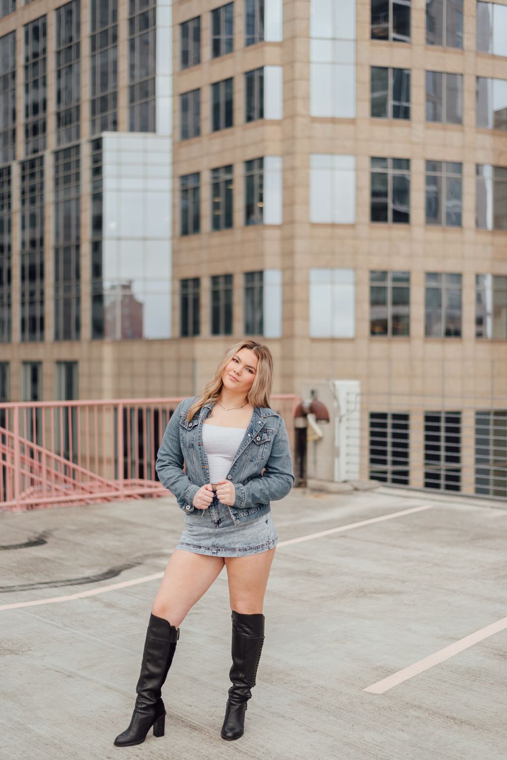 A casual street style look featuring knee-high boots, denim jacket and skirt against an urban office building backdrop.