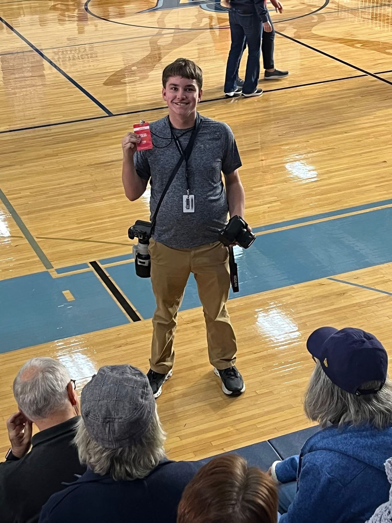 Professional photographer standing in a gymnasium holding camera equipment and a beverage.