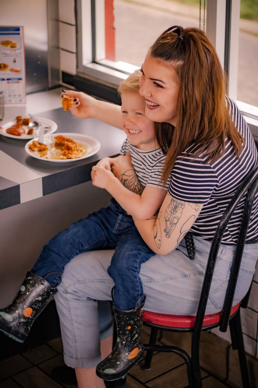 Person in striped shirt and jeans sitting at a table enjoying a casual meal indoors.