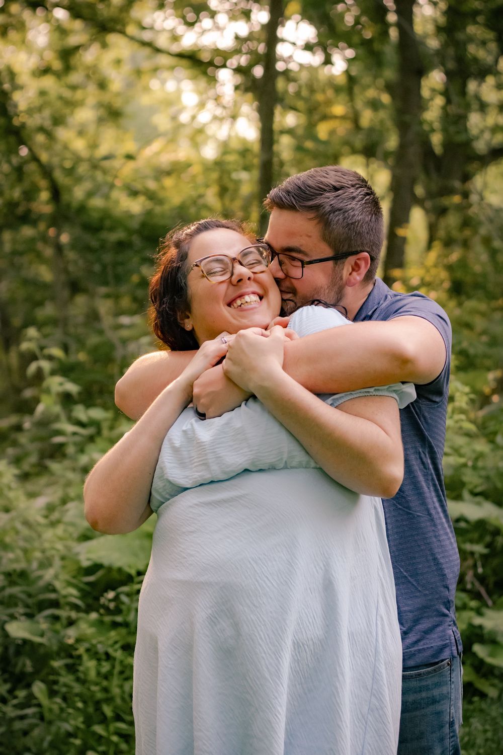 A joyful couple embracing outdoors in a wooded setting during golden hour.