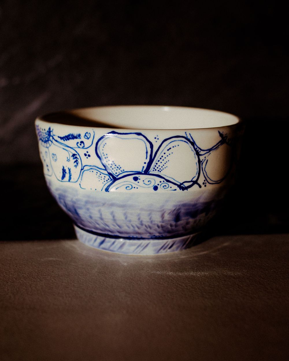 Handmade ceramic bowl with blue abstract patterns on white glaze against dark background.