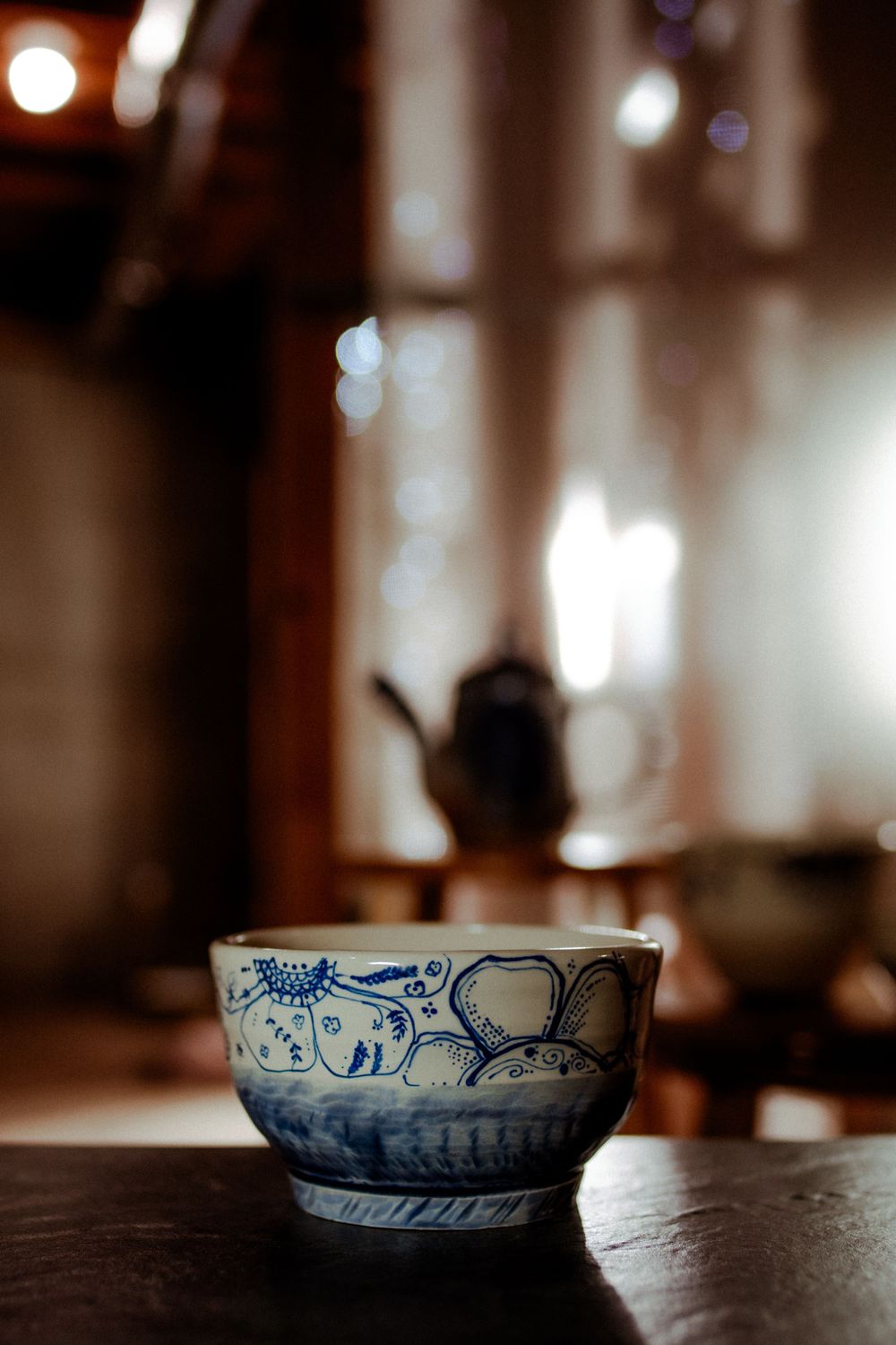 Antique blue and white porcelain tea cup on dark wood table with blurred teapot in background.