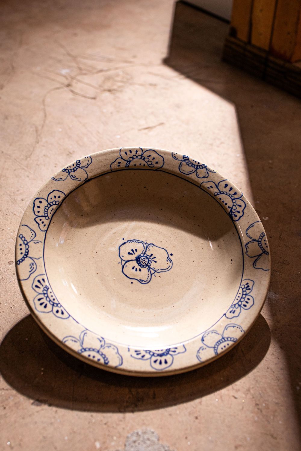 Cream ceramic bowl with blue flower center and floral border pattern on terracotta floor.