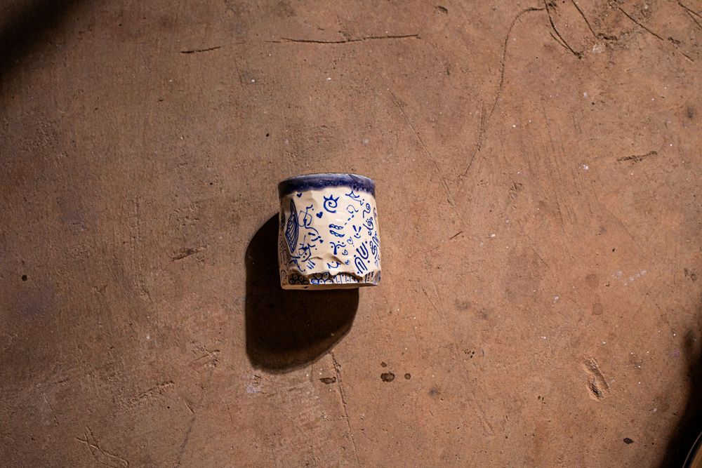 Small blue and white floral ceramic pot casting a shadow on a sandy terracotta surface.