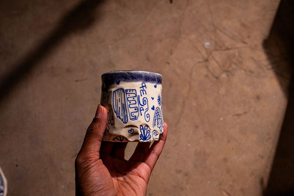 Hand holding a white ceramic cup with blue hand-drawn doodle illustrations and text.