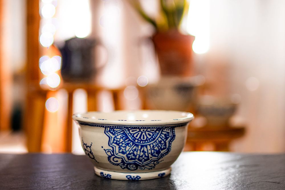 Blue and white ceramic bowl with intricate mandala pattern on dark stone surface with bokeh background.