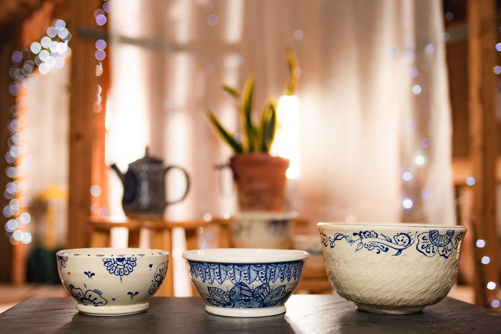 Three blue and white ceramic bowls in varying sizes arranged on dark surface with bokeh fairy lights.