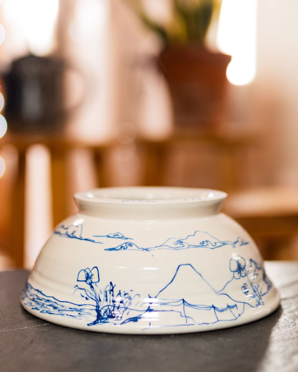 White ceramic bowl featuring blue hand-painted mountain and floral landscape art.