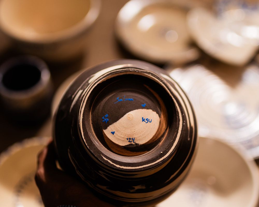 Bottom view of a dark glazed ceramic bowl with blue handwritten KSU text and yin-yang design.