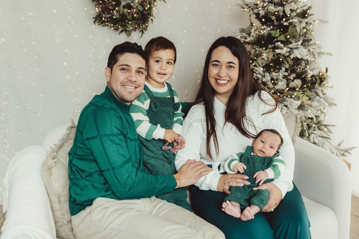 Family holiday portrait session with coordinated green outfits against white backdrop.