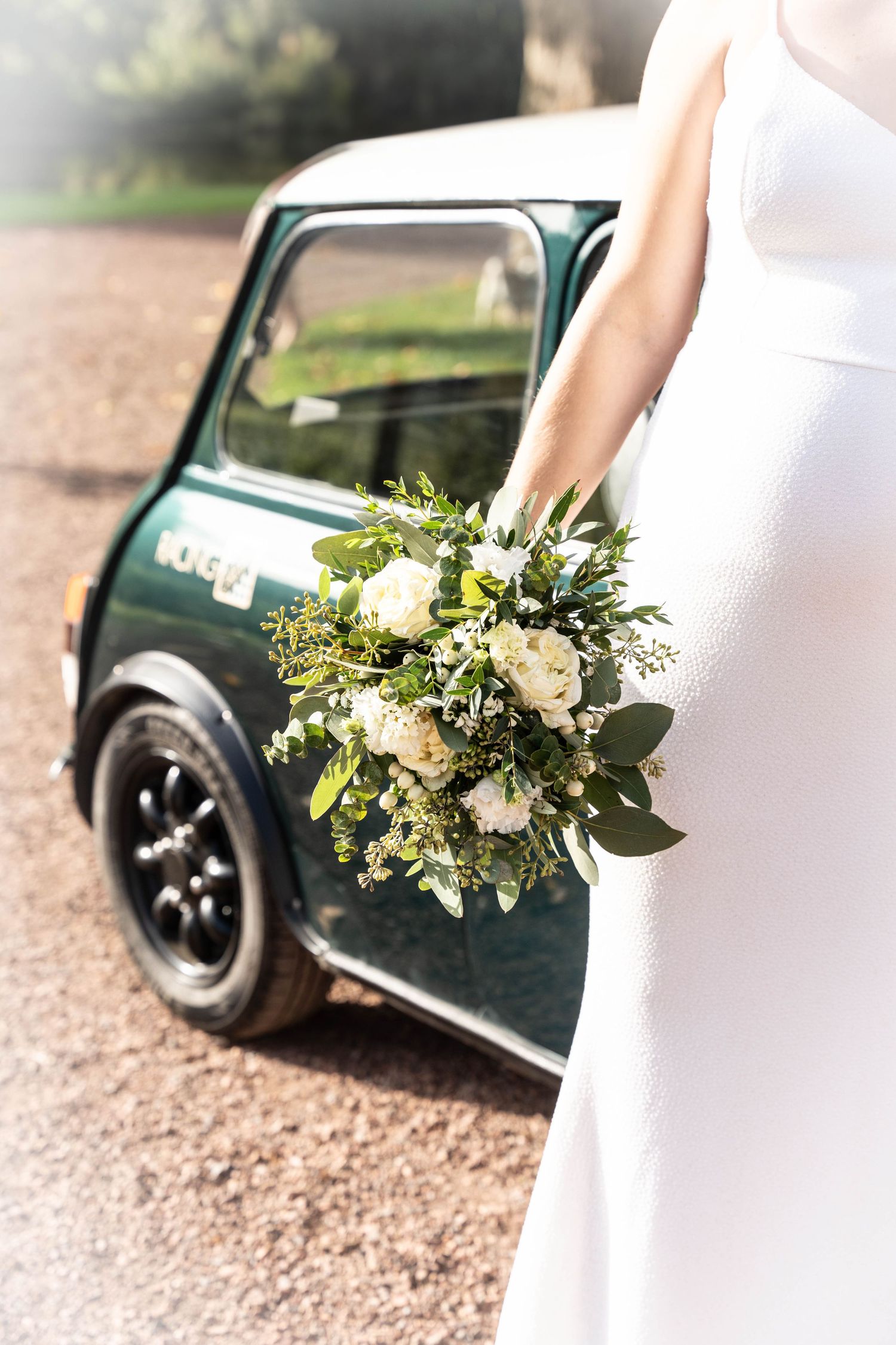 Wedding bouquet with white flowers and greenery against classic green Mini Cooper.