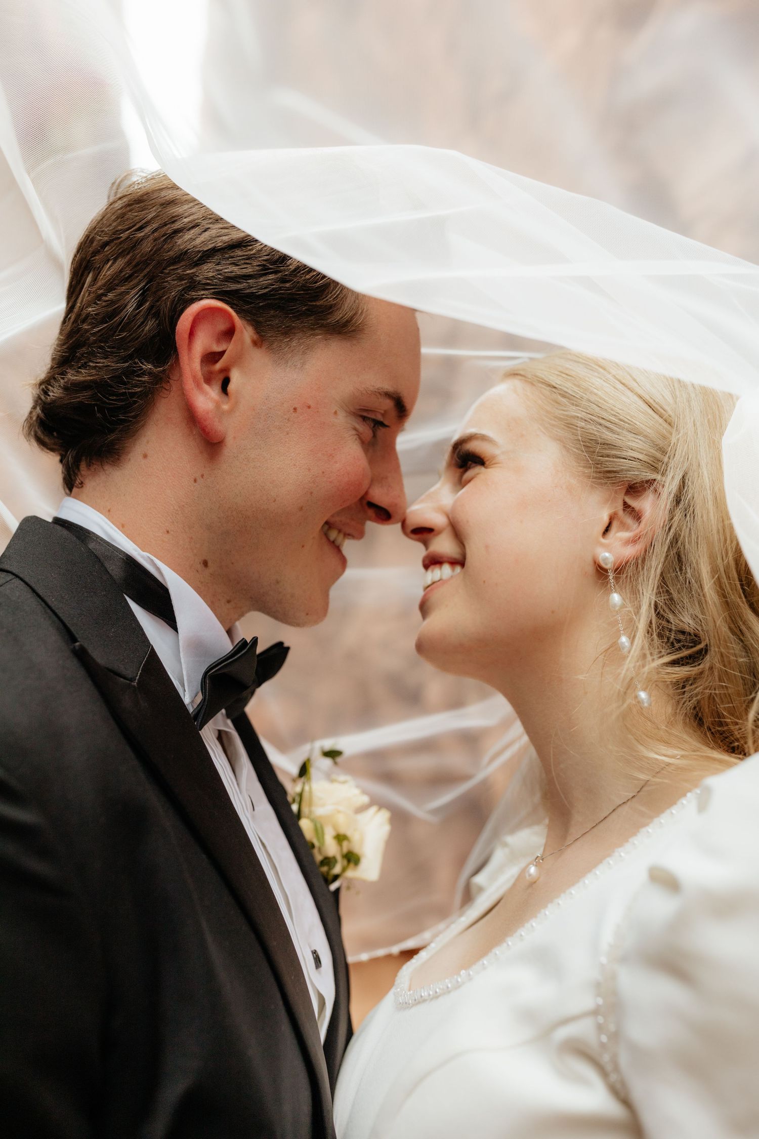 Bride and groom smiling nose to nose under a flowing veil on their wedding day.