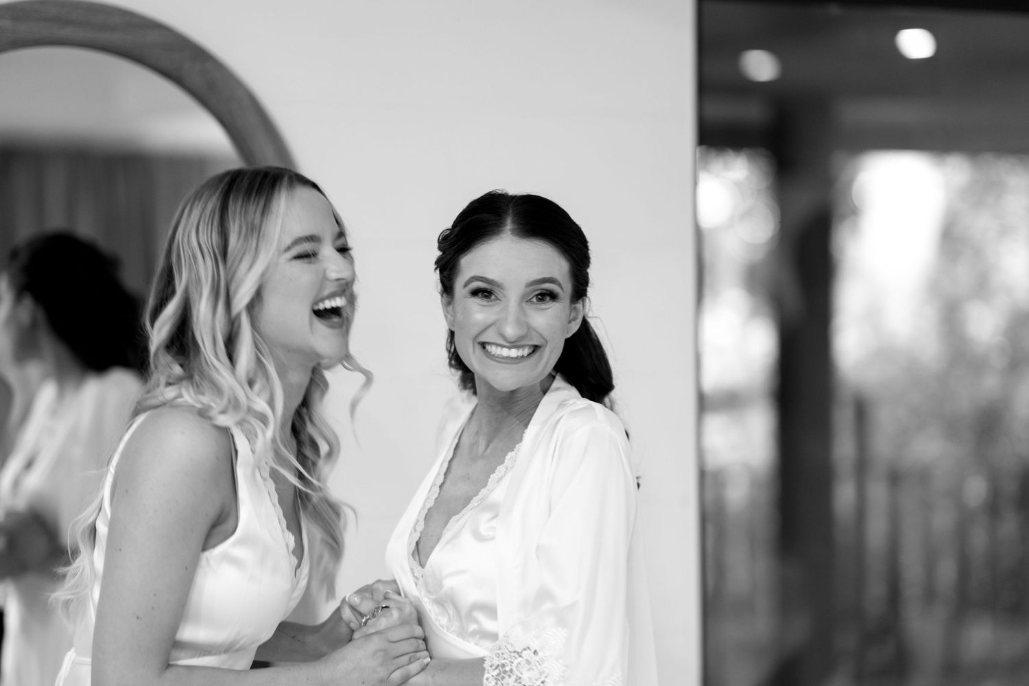 Black and white photo of two women embracing and laughing while getting ready.