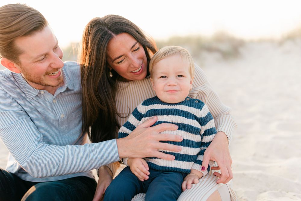 A family of three wearing cozy sweaters on the beach in September while having photos taken by Monmouth County photographer in sea girt, nj.
