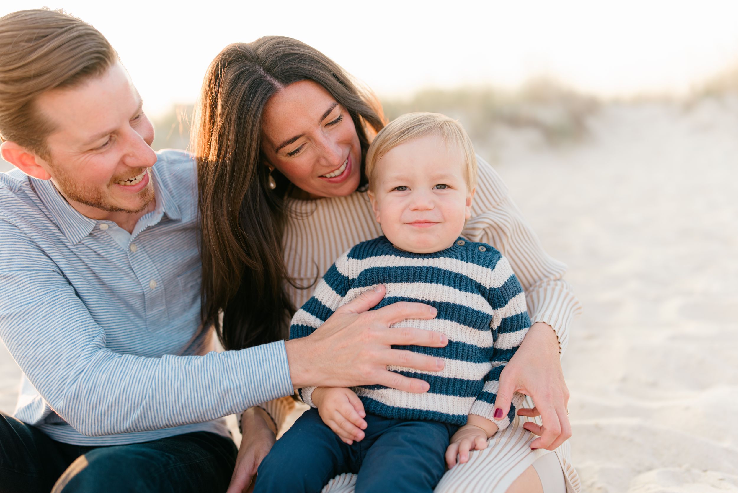 A family of three wearing cozy sweaters on the beach in September while having photos taken by Monmouth County photographer in sea girt, nj.