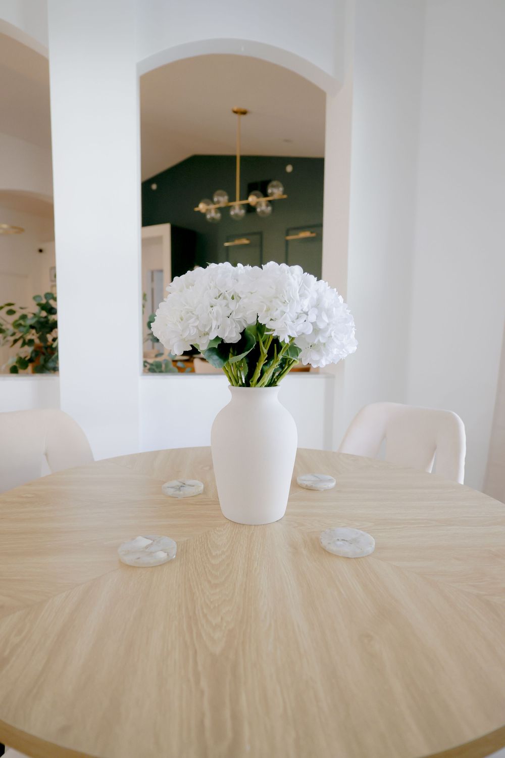 Elegant groom in black tuxedo seated on blue velvet chair near window.