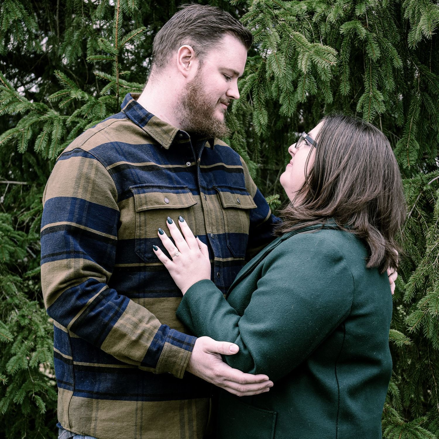 An intimate portrait of a couple embracing against a backdrop of evergreen trees.