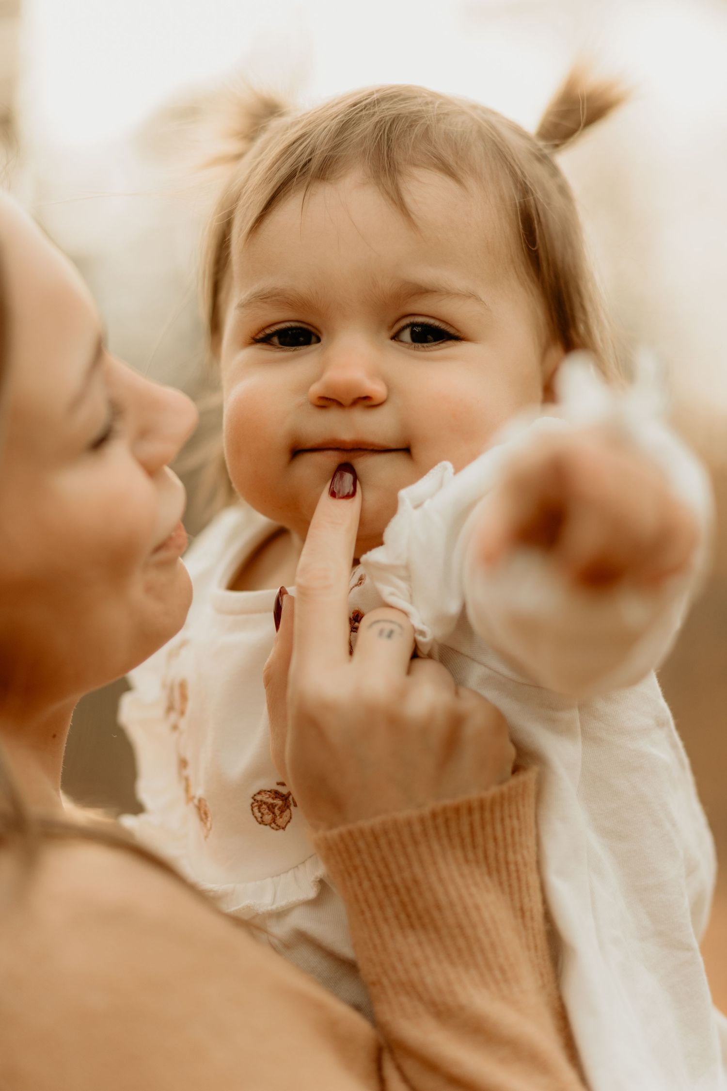 Mother and baby share tender playful moment in warm sepia tones.