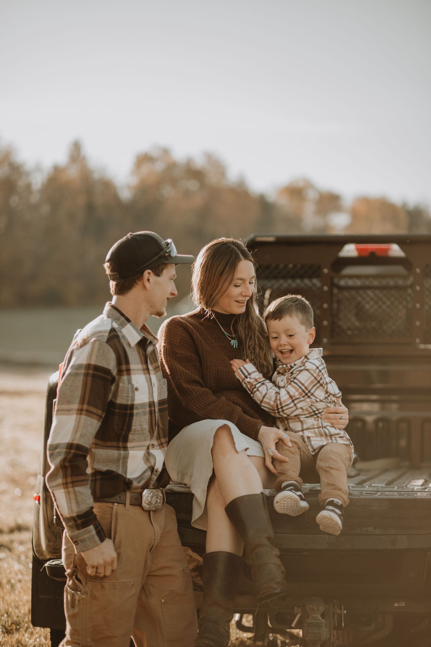 Family enjoys autumn afternoon together on back of pickup truck in warm golden light.