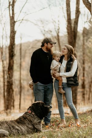 Family and their black dog enjoy an autumn walk together in the woods.