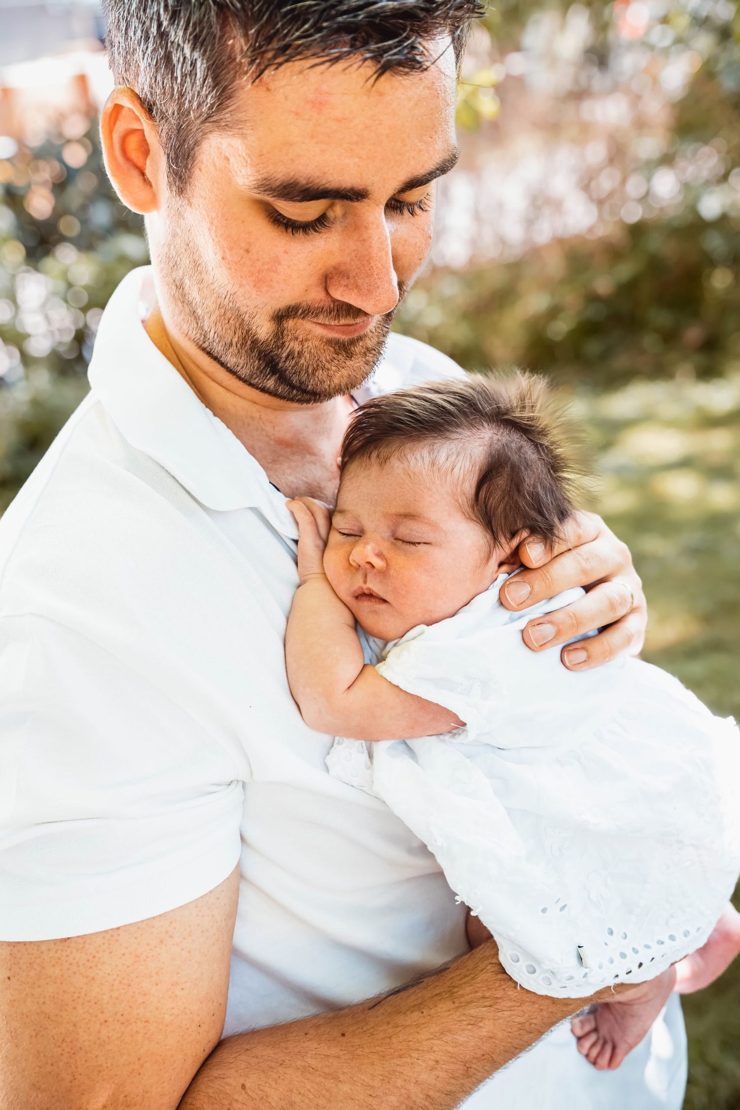 Tender moment between parent and sleeping infant in white clothing.