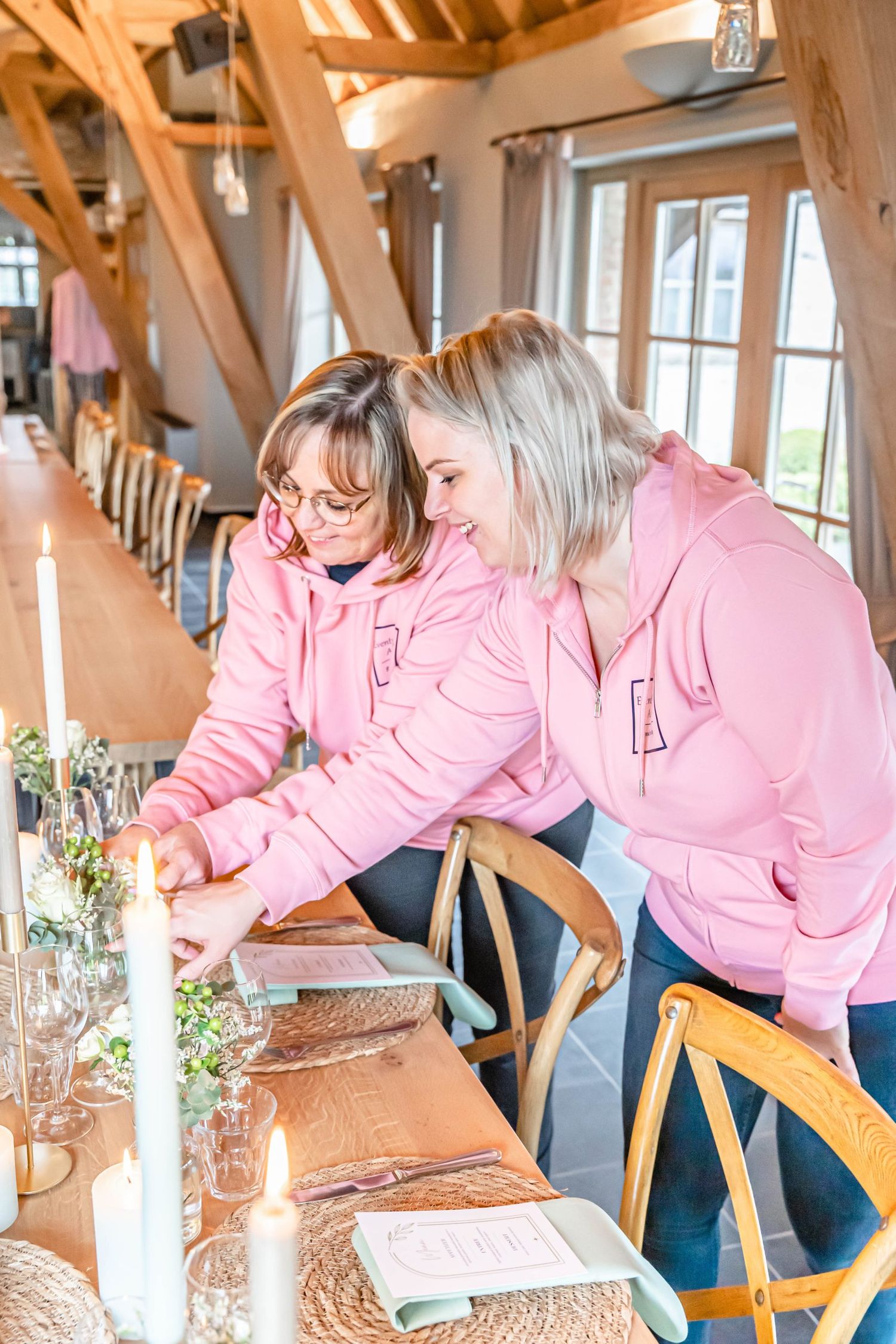 Event setup scene showing two people in matching pink hoodies arranging table settings with candles.