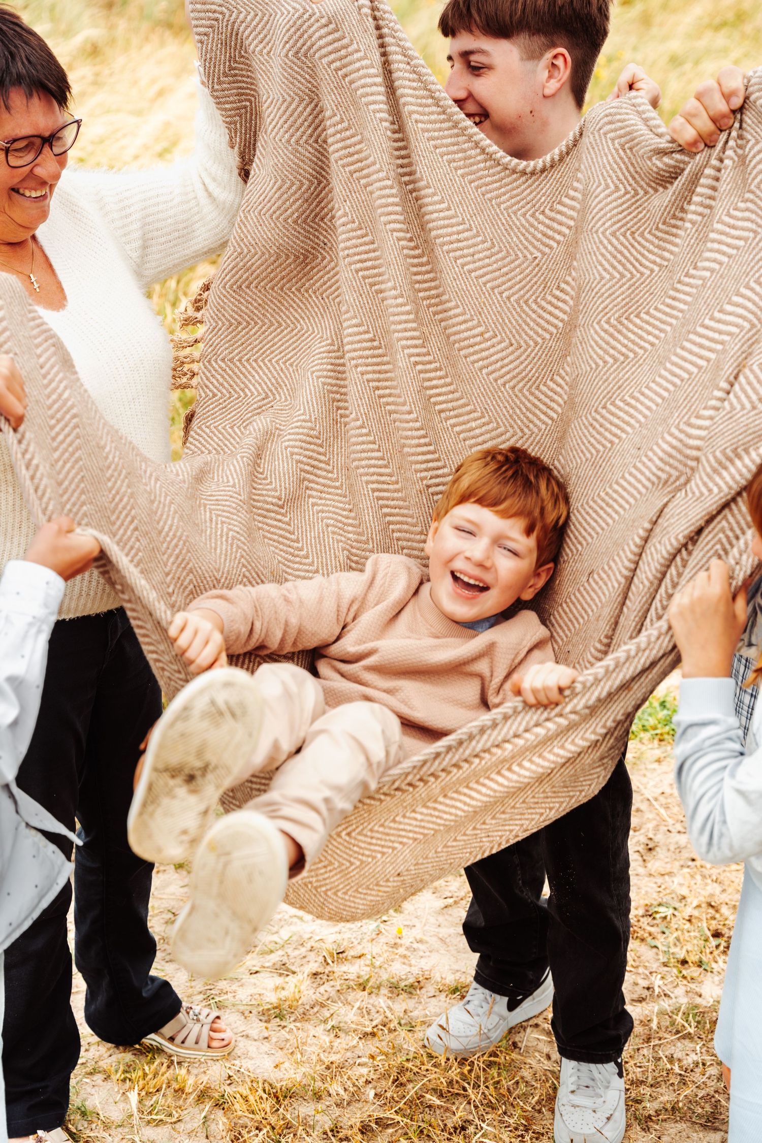 Children laughing while being swung in a beige blanket outdoors.