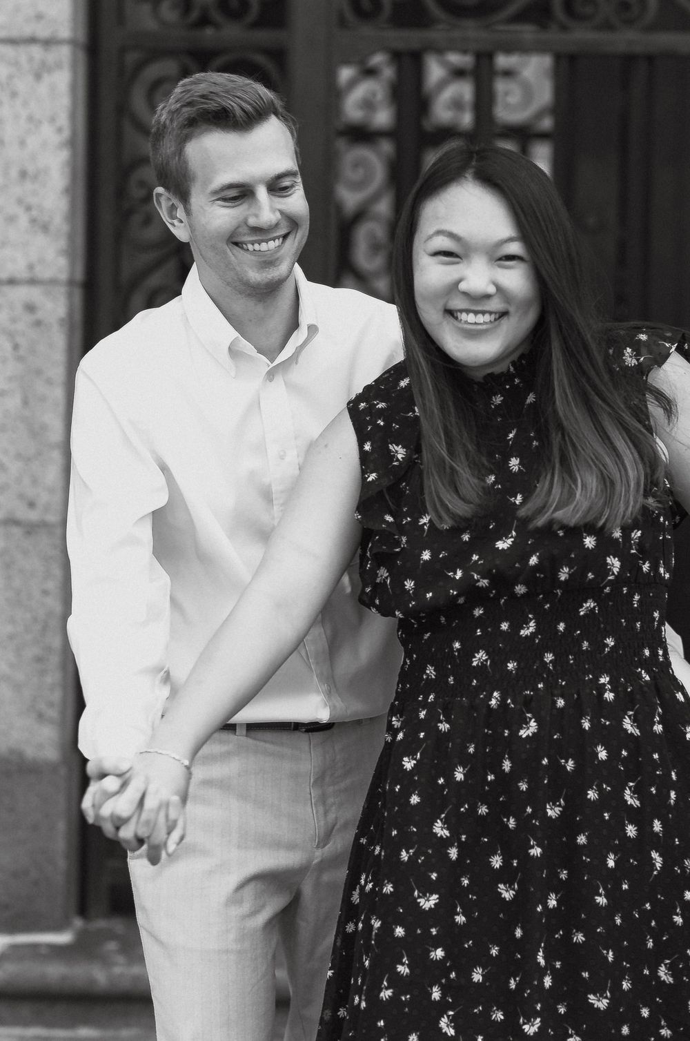 Black and white photo of a smiling couple holding hands outside an ornate building entrance.
