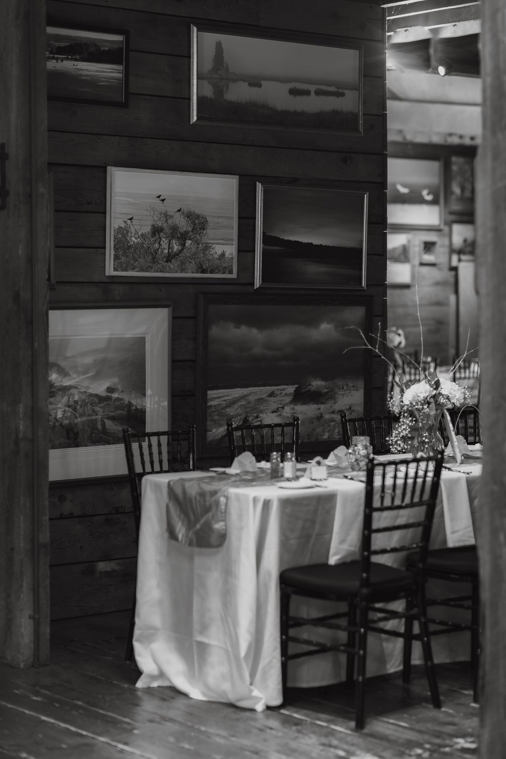Black and white photo of an elegant sweetheart table set for two in a rustic barn venue.