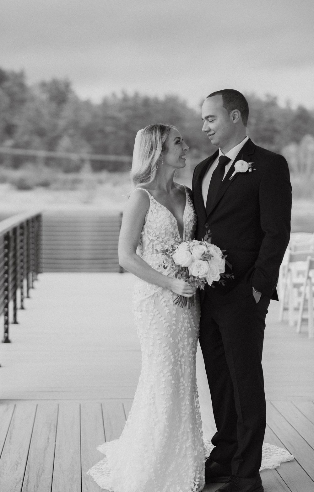 Black and white photo of bride and groom sharing a loving gaze on a wooden deck at their outdoor wedding.