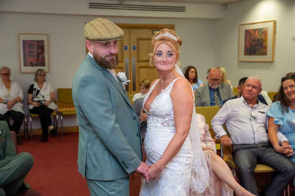 Bride and groom hold hands and smile during an intimate civil wedding ceremony indoors.